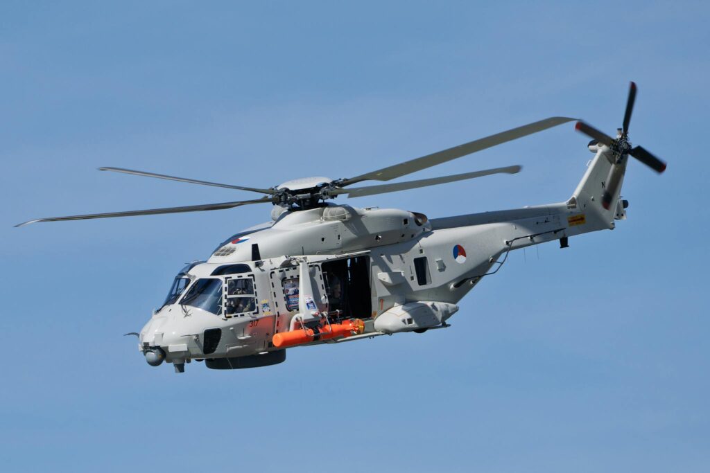 A military helicopter flying mid-air with open doors, showcasing its equipment against a clear blue sky.